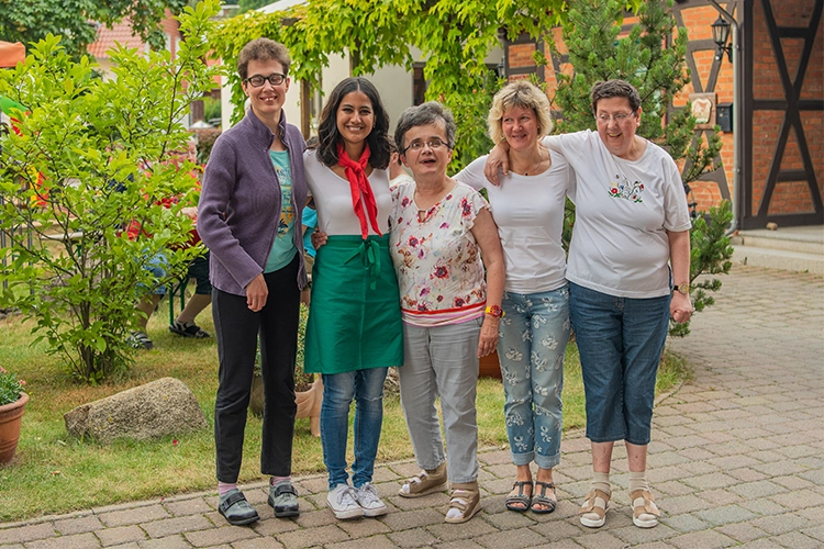 Fünf Frauen stehen Arm in Arm im Garten und lächeln