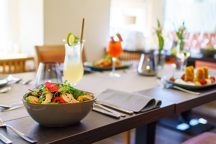 Gedeckter Restauranttisch mit frischem Salat, Getränken und weiteren Speisen im Hintergrund