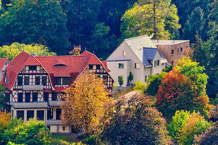 Historische Fachwerksvilla mit rotem Dach und moderner Erweiterung, eingebettet in herbstliche Parklandschaft