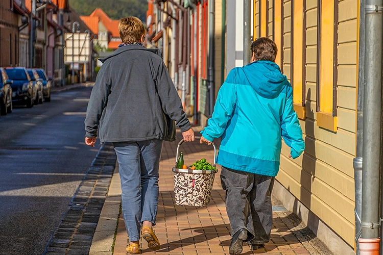Zwei Menschen gehen mit Einkaufskorb durch eine Wohnstraße