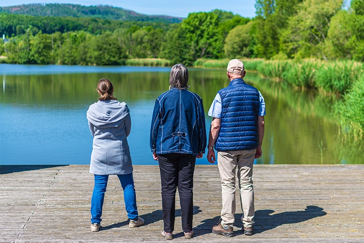 Drei Menschen stehen gemeinsam am See und schauen auf das Wasser