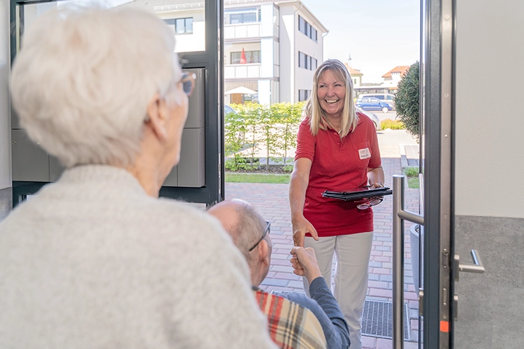 Pflegekraft begrüßt zwei ältere Menschen an der Wohnungstür