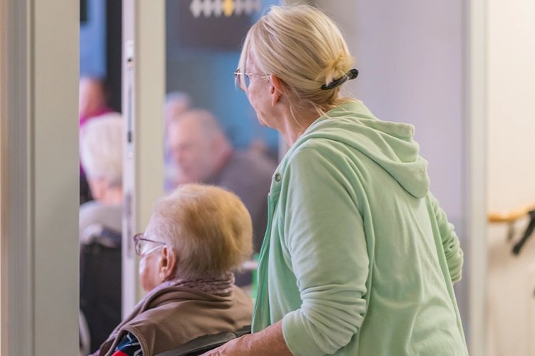 Betreuerin schiebt Seniorin im Rollstuhl