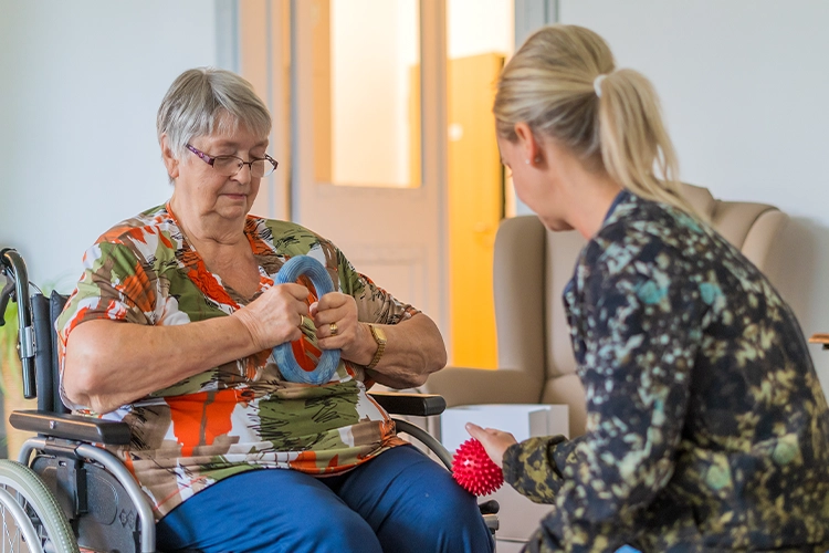 Seniorin trainiert mit einer Therapeutin ihre Handmotorik im Rollstuhl