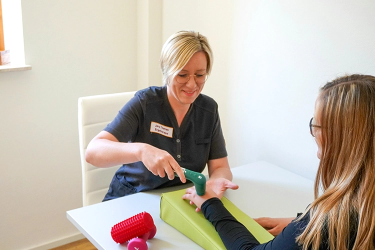 Ergotherapeutin behandelt Hand einer Patientin mit Therapiegerät