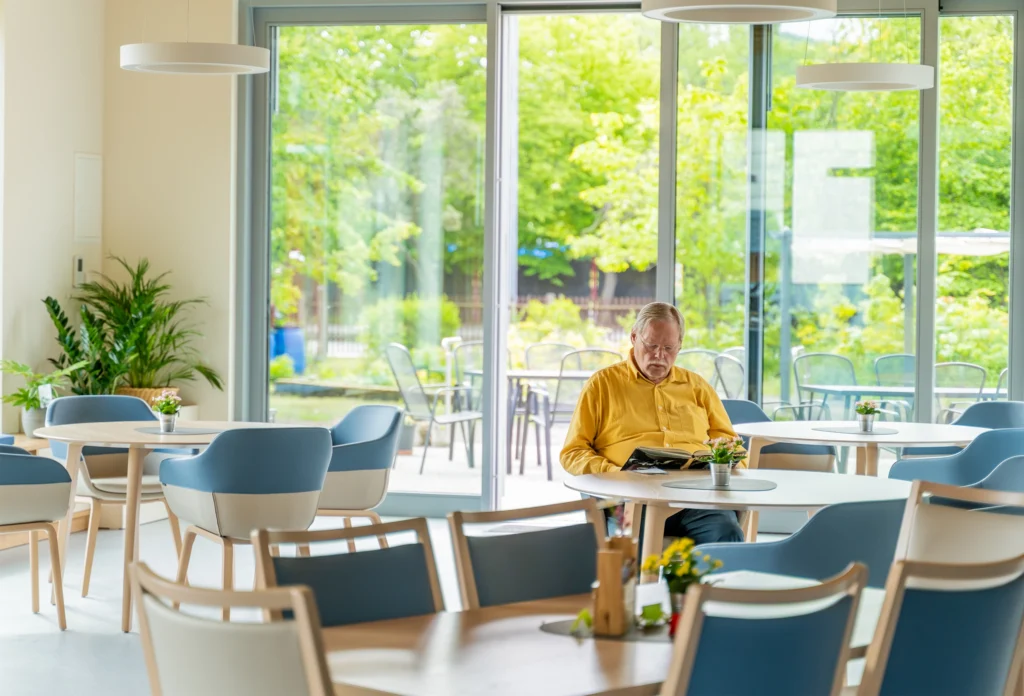 Senior sitzt allein in hellem Aufenthaltsraum und liest