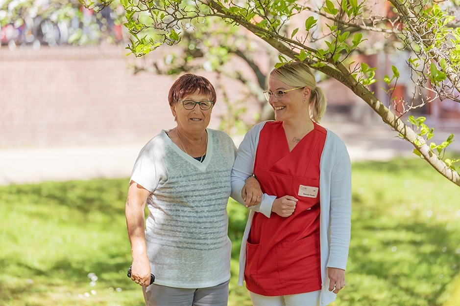 Seniorin und Pflegerin spazieren gemeinsam im Garten