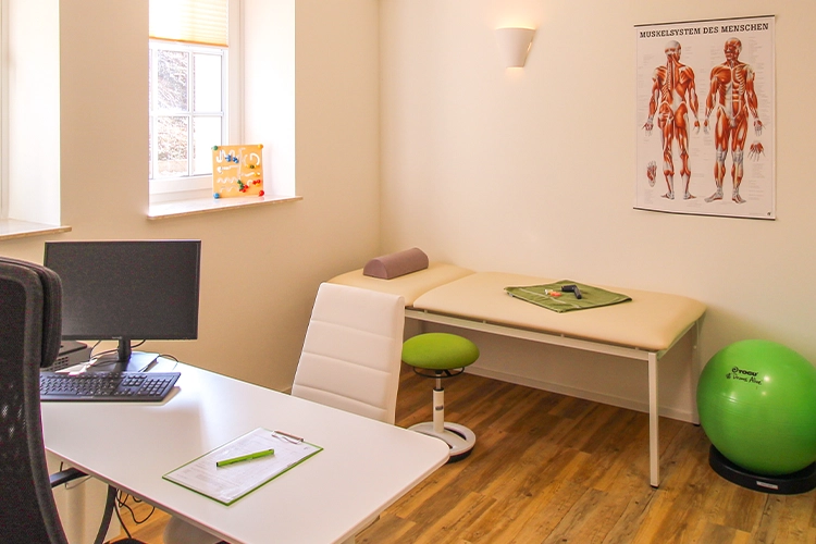 Behandlungsraum mit Liege, Schreibtisch und Gymnastikball