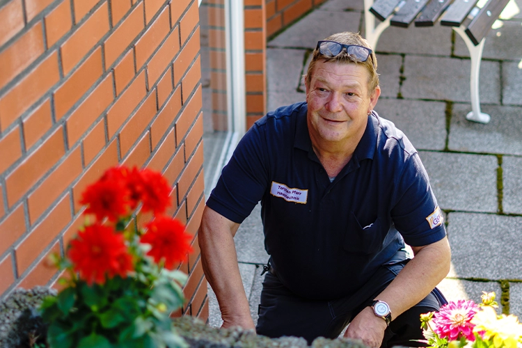 Mitarbeiter pflegt Blumenbeet im Außenbereich einer Einrichtung