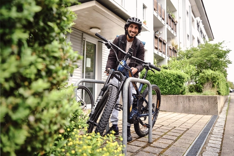 Mitarbeiter stellt ein Fahrrad vor einem Gebäude ab und lächelt.