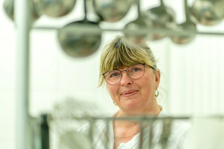 Mitarbeiterin blickt durch Küchenutensilien und lächelt in die Kamera