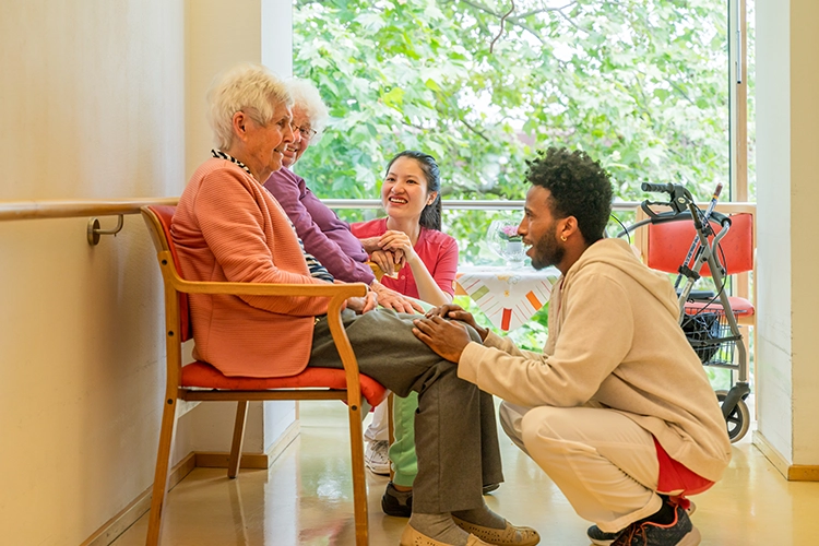 Pflegekräfte sprechen mit zwei Seniorinnen im Aufenthaltsraum