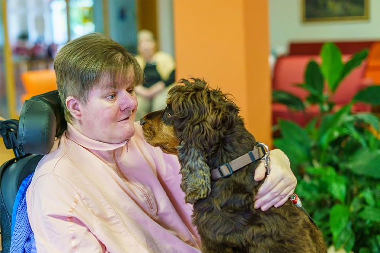Patientin im Rollstuhl erhält liebevolle Zuwendung von einem Therapiehund