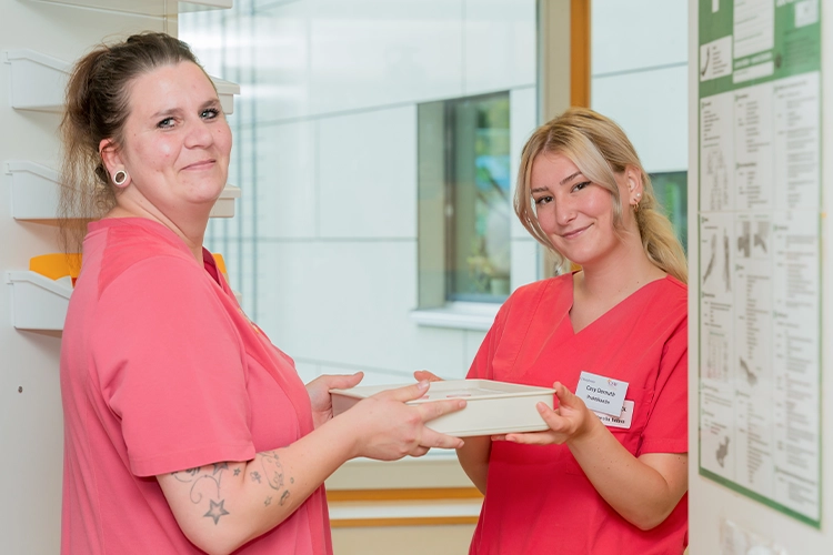 Zwei Pflegekräfte übergeben gemeinsam Dokumente und lächeln