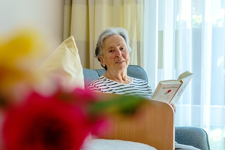 Ältere Frau sitzt im Sessel und liest ein Buch