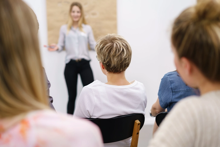 Dozentin steht vor einer Gruppe und erklärt Inhalte während einer Schulung