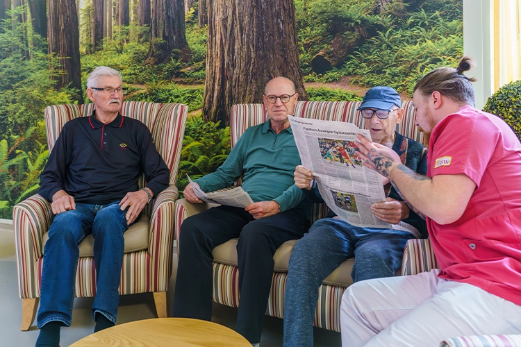 Männer lesen gemeinsam Zeitung mit Betreuer
