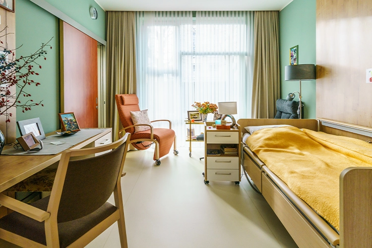 Helles Zimmer mit Bett, Sessel und Tisch mit Stuhl