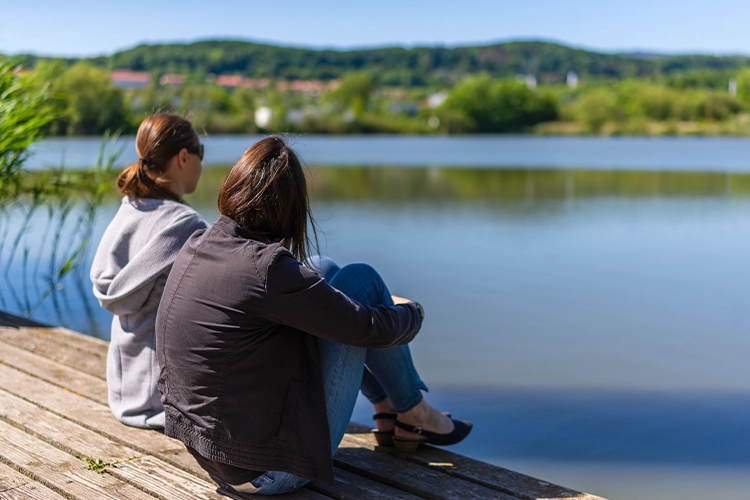 Zwei Personen sitzen am See und sprechen