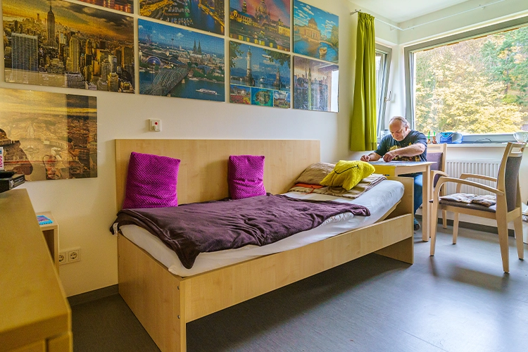 Einzelzimmer mit Bett, Tisch und Bildern