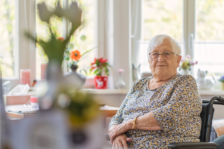 Ältere Frau sitzt im Rollstuhl in einem wohnlichen Zimmer