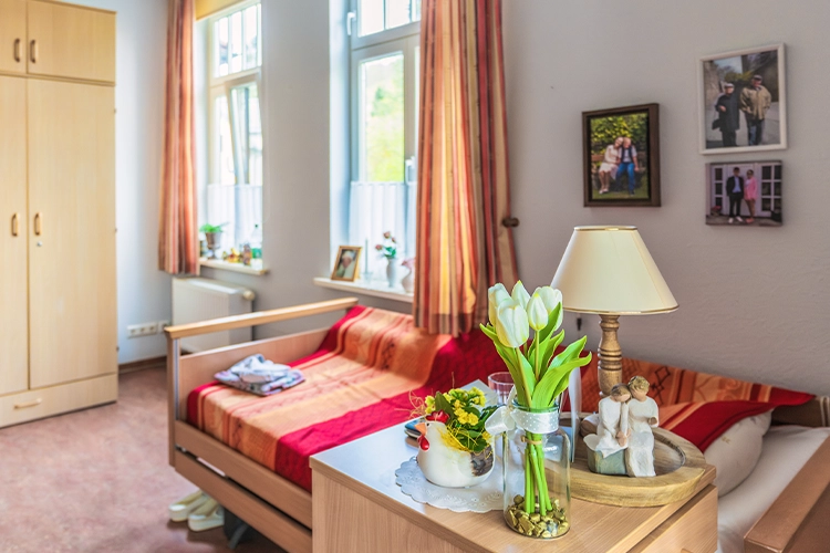 Helles Bewohnerzimmer mit Bett, Blumen und persönlichen Fotos