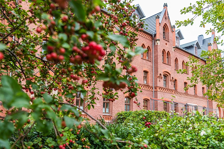 Backsteingebäude mit Garten und Bäumen im Vordergrund