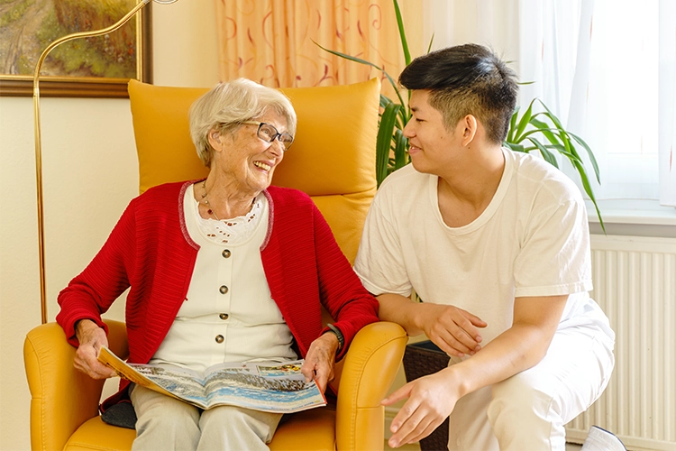 Seniorin im Sessel und Pfleger im Gespräch
