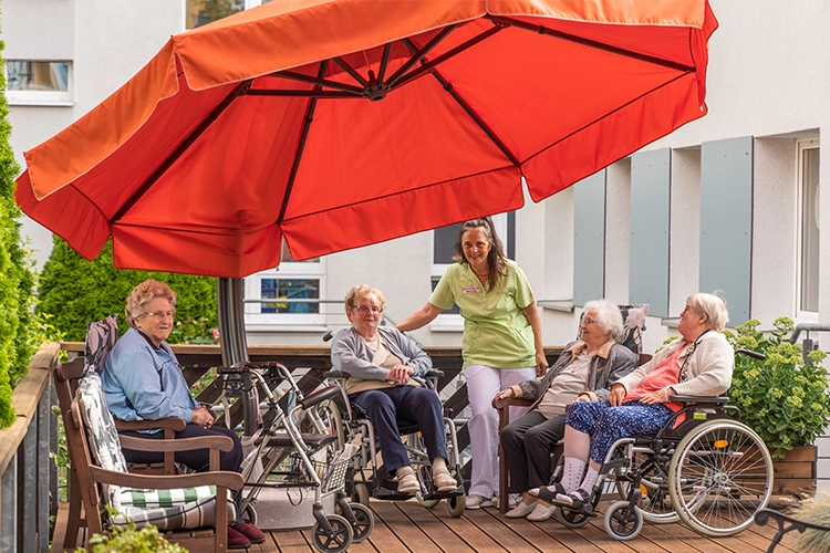 Senioren sitzen auf Terrasse mit Betreuung