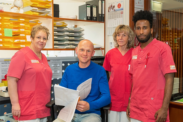 Vier Pflegekräfte in roter Arbeitskleidung stehen gemeinsam an der Pflegestation