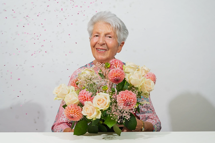 Ältere Dame hält einen Blumenstrauß mit Rosen und lächelt