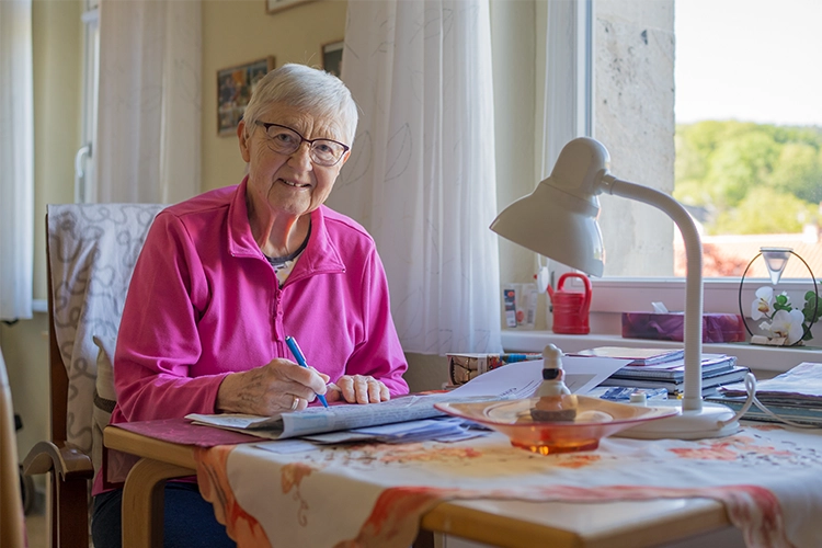 Ältere Dame in pink sitz lächelnd an ihrem Schreibtisch am Fenster