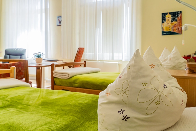Helles Doppelzimmer mit zwei grünen Betten, Tisch und Stühlen