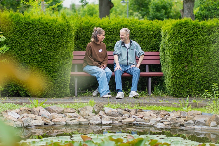 Frau und Mann sitzen lachend auf einer Bank im Park mit Teich.