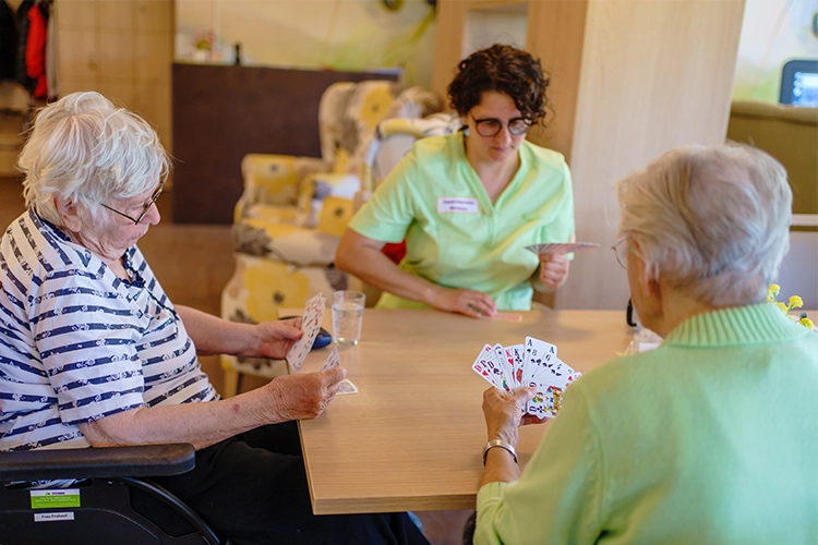 Betreuerin spielt gemeinsam mit zwei Seniorinnen Karten am Tisch