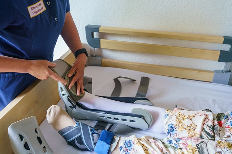 Physiotherapeutin behandelt das Bein einer liegenden Patientin am Pflegebett