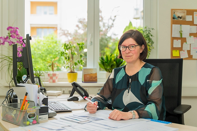Frau mit Brille sitzt an ihrem Büroschreibtisch mit Computer und Unterlagen