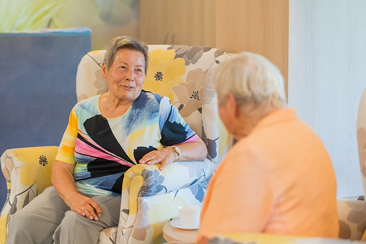 Zwei Seniorinnen sitzen in Sesseln und unterhalten sich angeregt