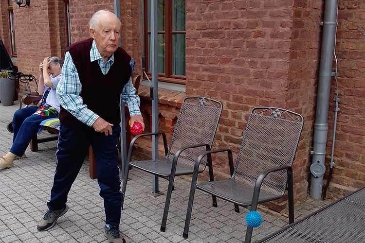 Älterer Herr wirft einen blauen Ball beim Spiel auf einer Terasse.