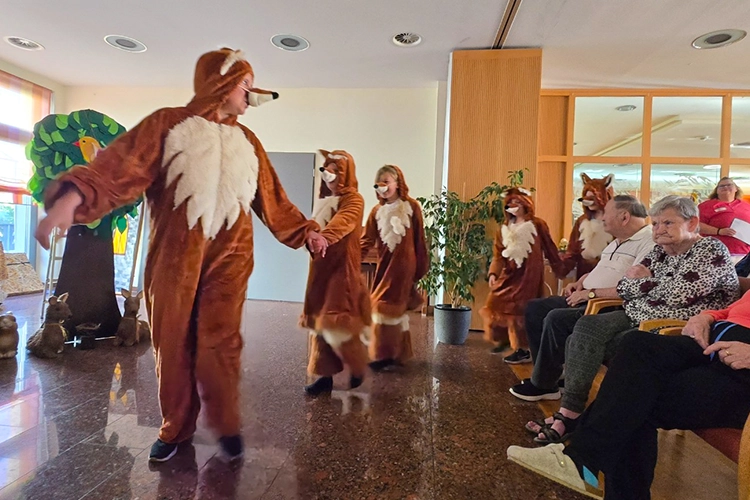 Darsteller in Fuchskostümen laufen tanzend an sitzenden Zuschauern vorbei.