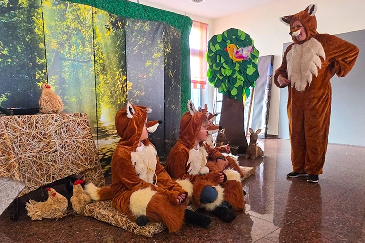 Kinder in Fuchskostümen sitzen auf Strohballen, ein Erwachsener im Fuchskostüm daneben.