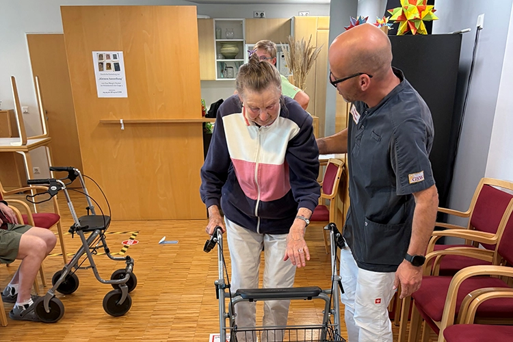Physiotherapeut unterstützt eine ältere Frau beim Gehen mit dem Rollator.