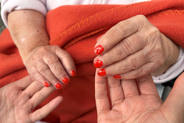 Nahaufnahme zweier älterer Hände mit frisch rot lackierten Fingernägeln.