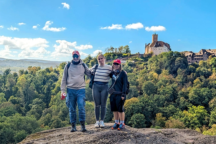 Drei Personen stehen auf einem Felsen mit Blick auf die Wartburg.