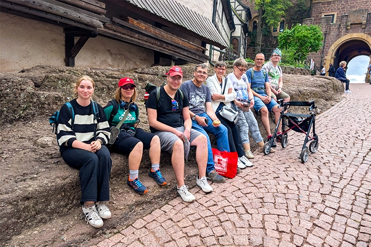 Achtköpfige Gruppe sitzt auf einer Steinbank vor der Wartburg.