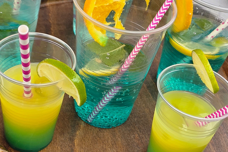Vier Becher mit Cocktails, Strohhalmen und Zitronen- und Orangenscheiben.