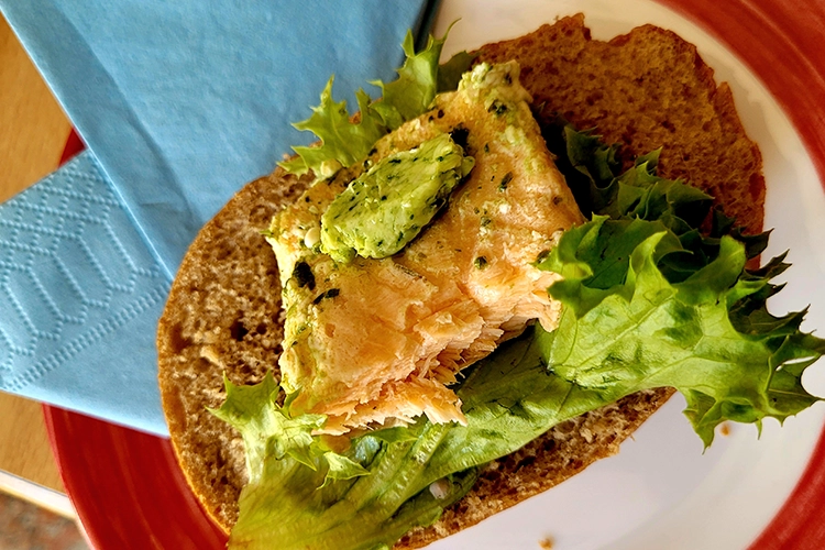 Vollkornbrötchen mit Fisch, Kräuterbutter und Salatblatt auf rotem Teller.
