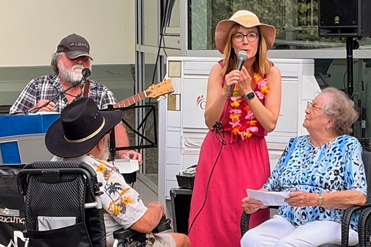 Frau mit Hut und Blumenkette singt, Gitarrist daneben.
