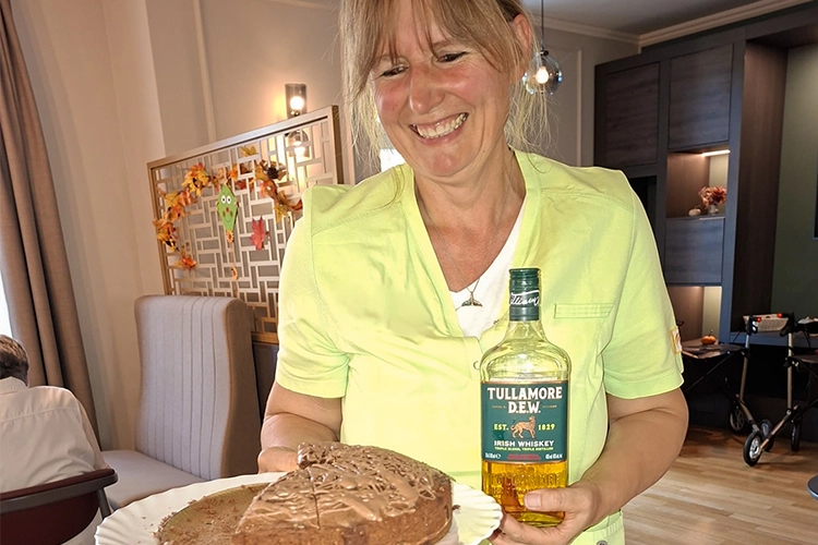 Lächelnde Betreuerin hält Kuchen und Flasche Tullamore Dew Whiskey.