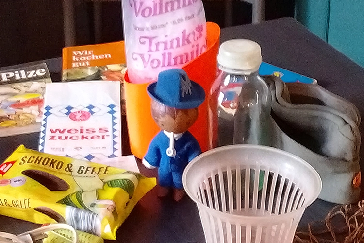 DDR-Produkte auf einem Tisch: Trinkvollmilch, Weisszucker, Schoko & Gelee und blaue Figur.